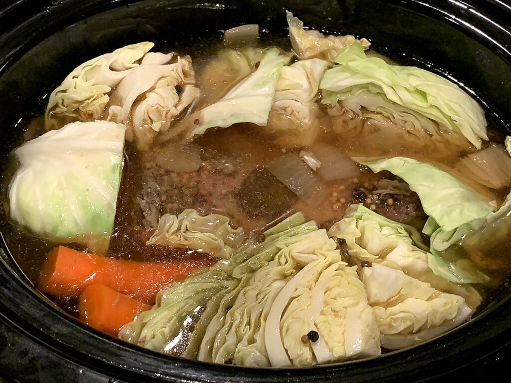 Cabbage wedges have been added to the corned beef, onions and carrots in the slow cooker.