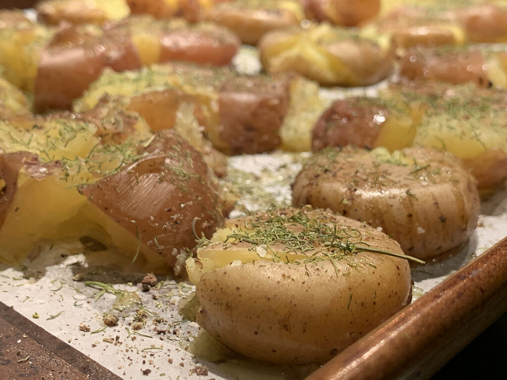 Close up view of slightly smashed baby potatoes sprinkled with dill. All on a sheet pan. 