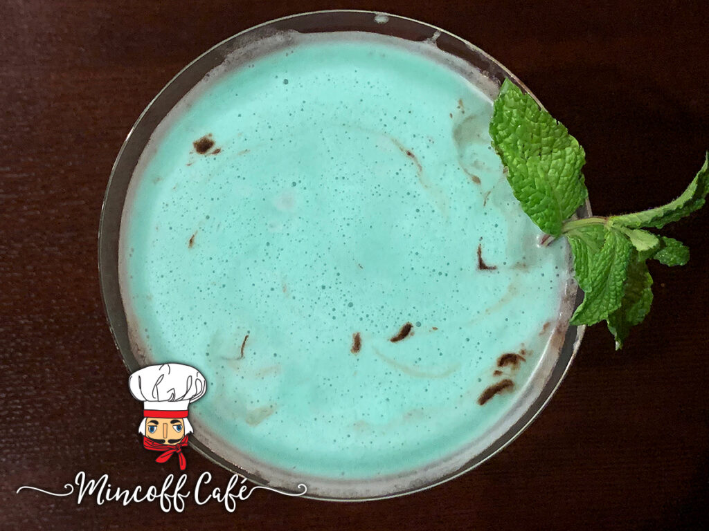Overhead view of a green cocktail with chocolate and garnished with mint leaves.
