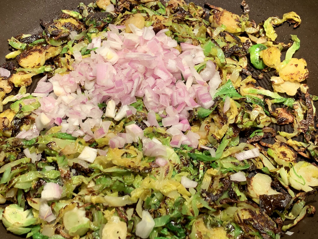 Slightly browned shredded brussles sprouts with a small pile of uncooked shallots on top.