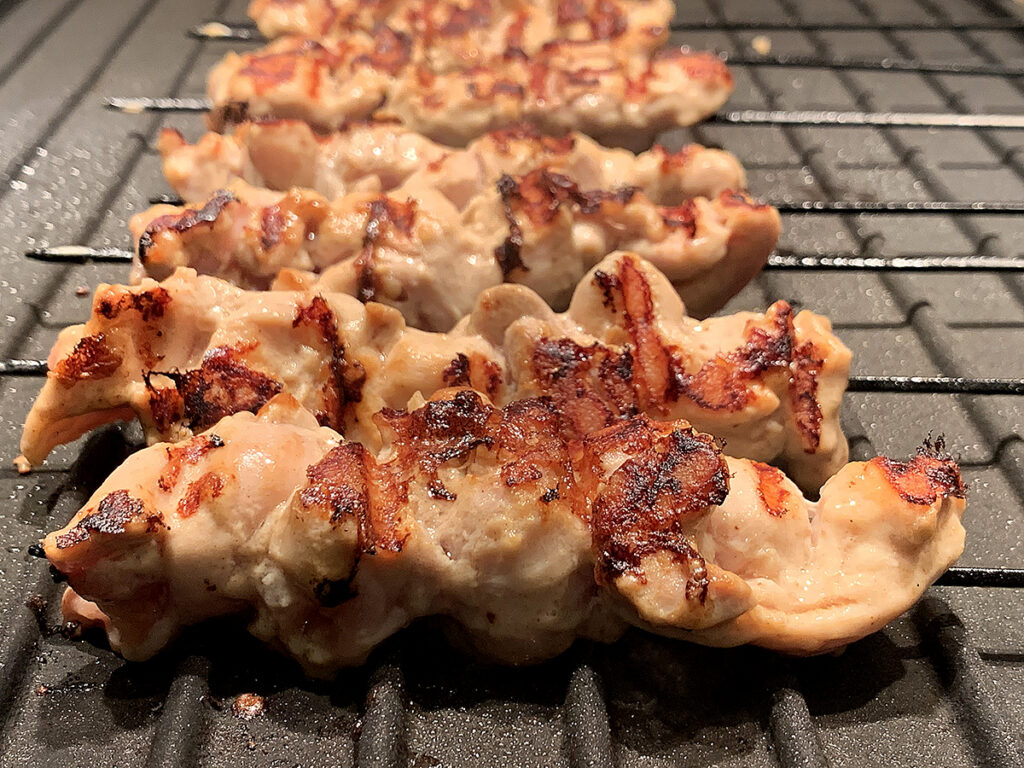 Charred chicken skewers on an indoor grill.