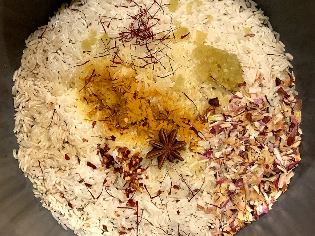 White rice in a grey pot with saffron, minced garlic, red pepper flakes, turmeric and dried shallots on top.
