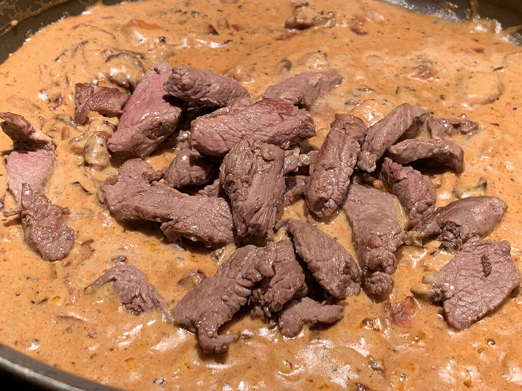 Tan sauce with small chunks of brown meat that is pink in the center, piled in the center of a skillet.