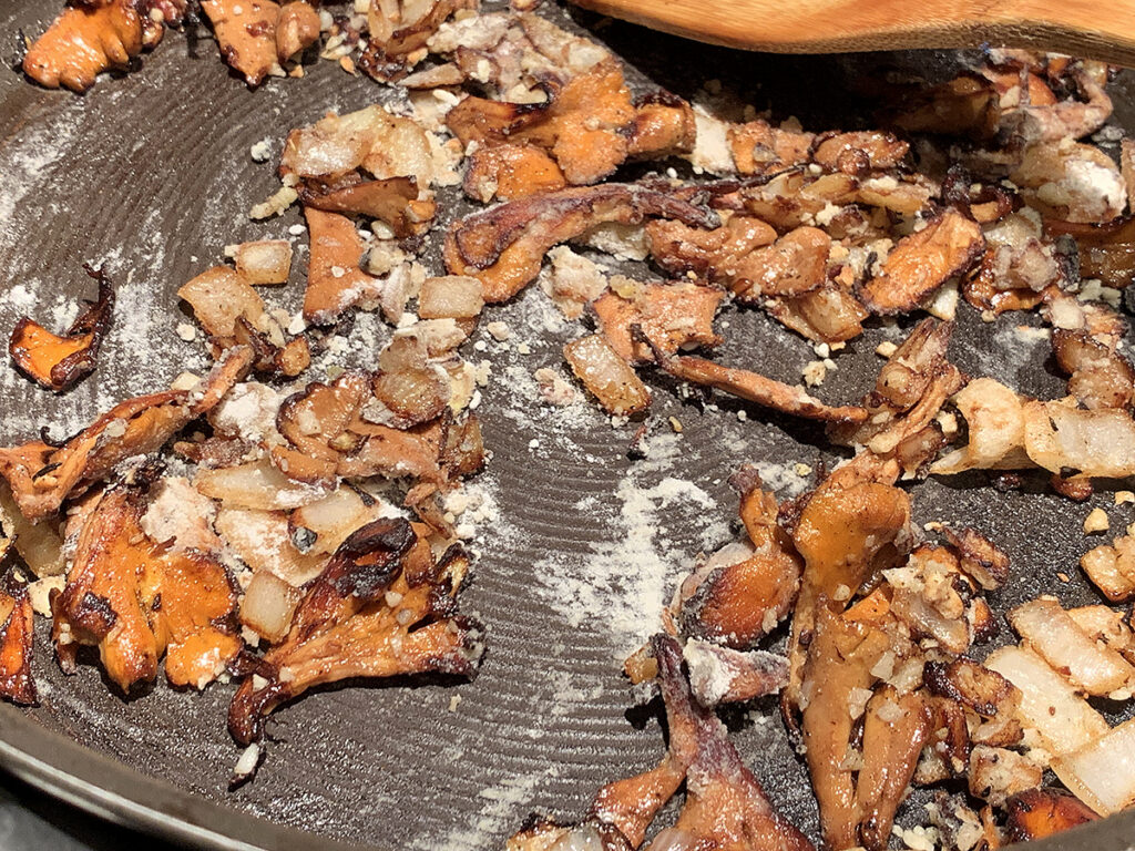 A small amount of flour added to chanterelle mushrooms and chopped onions sautéing in a skillet.