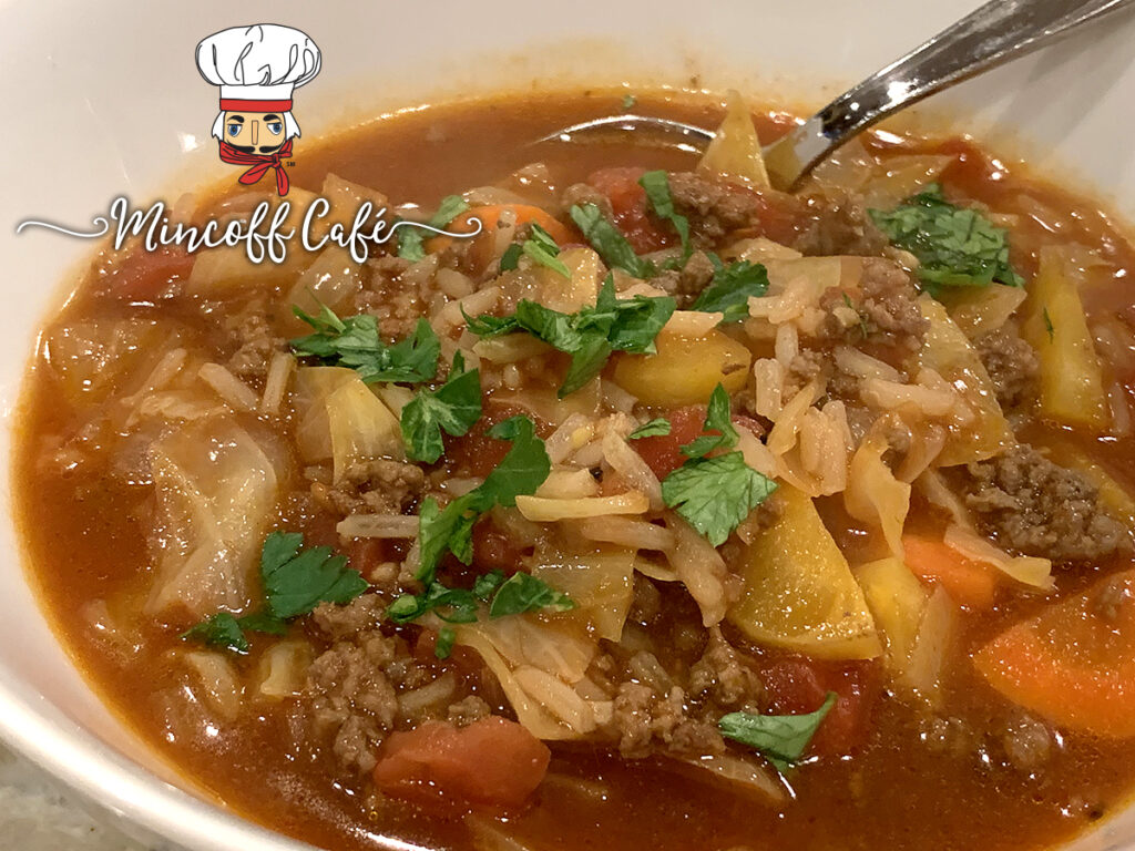 A bowl of cabbage roll soup with it's red broth and garnished with green parsley.