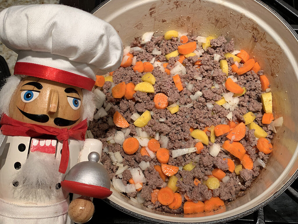 Orange and yellow carrots with onions and ground beef in a white dutch oven.