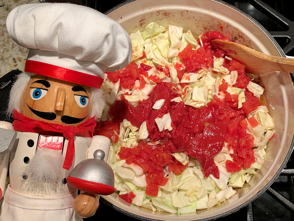 chopped green cabbage topped with chopped tomatoes in a white dutch oven. There's a nutcracker in the foreground who looks like a chef.