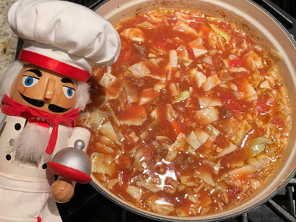 Cabbage roll soup with it's red broth. There's a nutcracker in the foreground who looks like a chef.