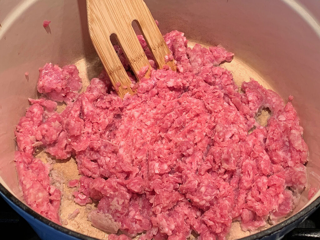 Rare ground beef in a white dutch oven with a wood spatula. 