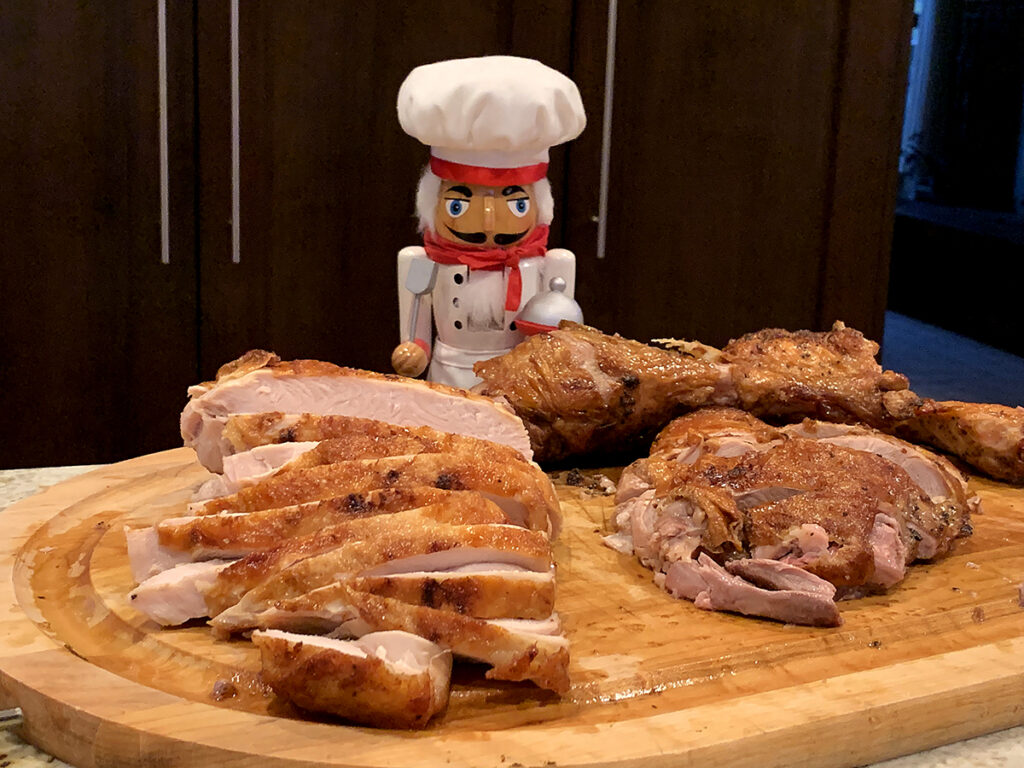 Sliced nicely browned white turkey meat on the left and dark meat on the right on a wood board. There's a nutcracker in the background who looks like a chef.