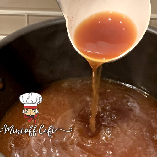 Dark brown turkey stock being poured out of a white ladle into a large stockpot.