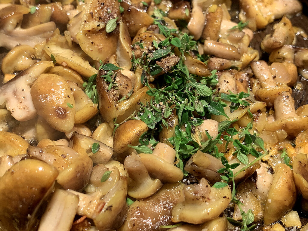 roughly chopped yellow mushrooms with fresh thyme in a skillet.