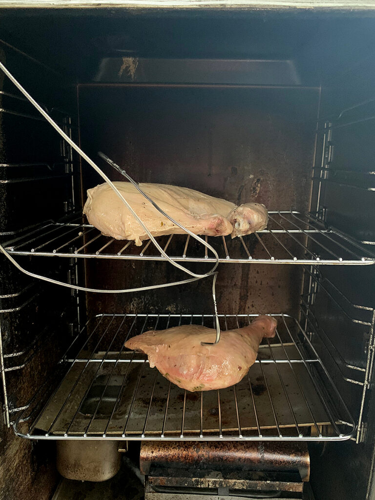 Turkey breast on the top shelf of a smoker and leg quarter on the bottom.