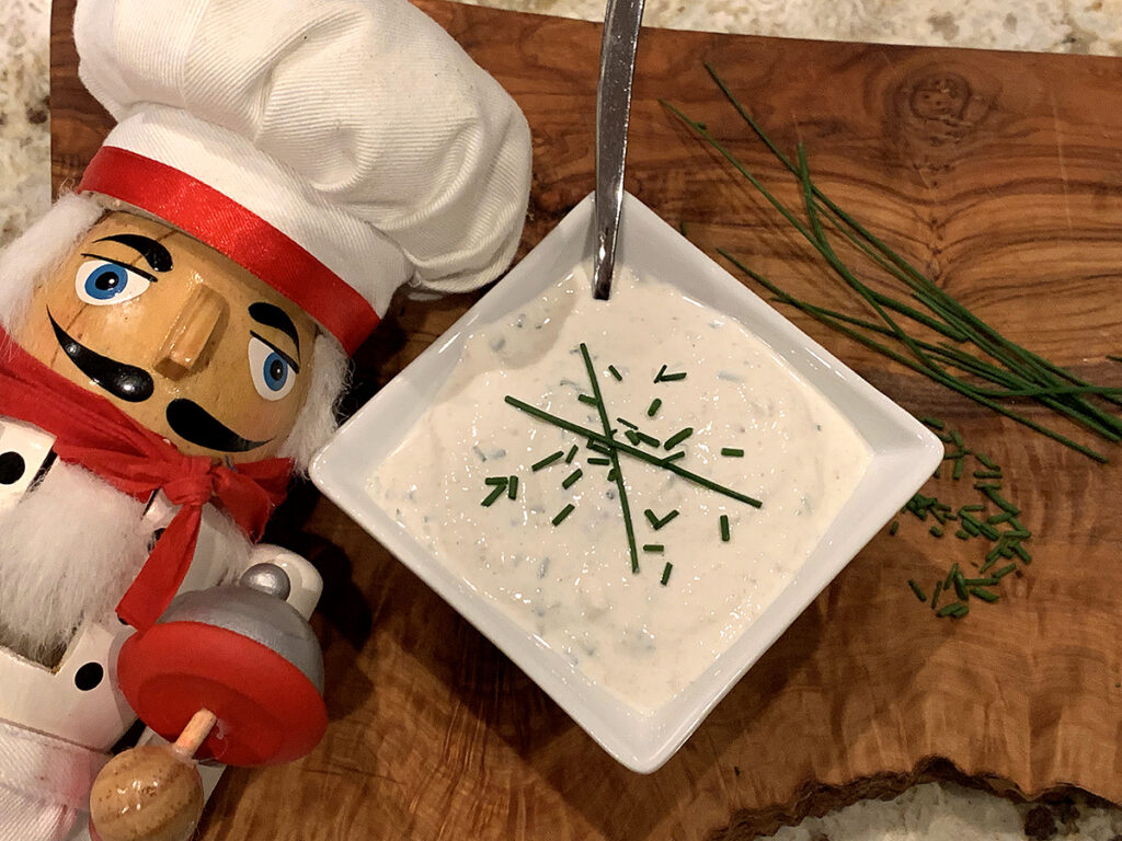 White sauce in a square white ramekin, sprinkled with chives. There's a nutcracker in the foreground who looks like a chef.