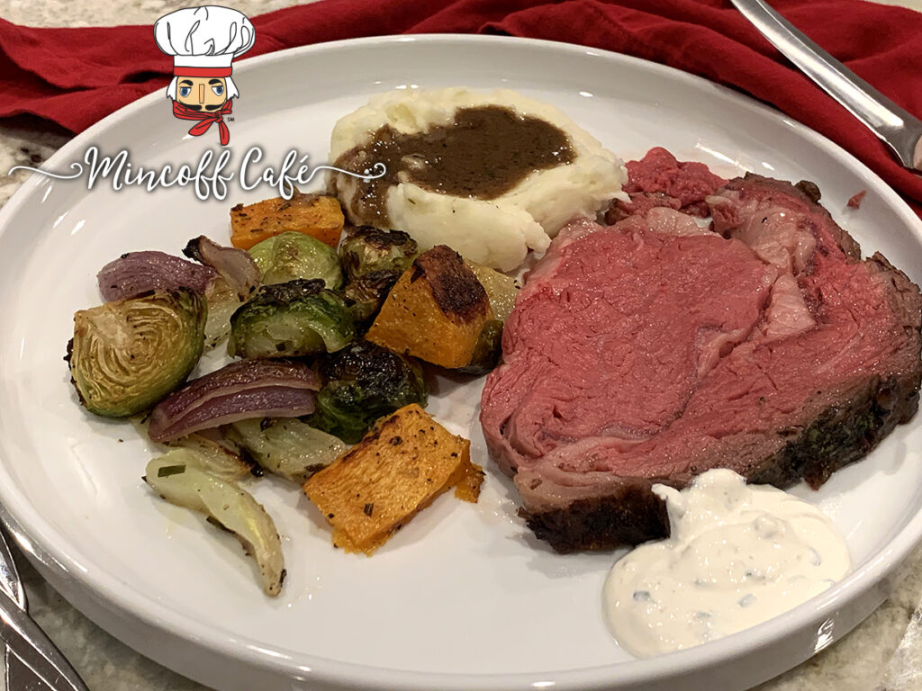 Medium rare slice of prime rib roast with roasted colorful veggies and mashed potatoes with gravy on a white  plate. 