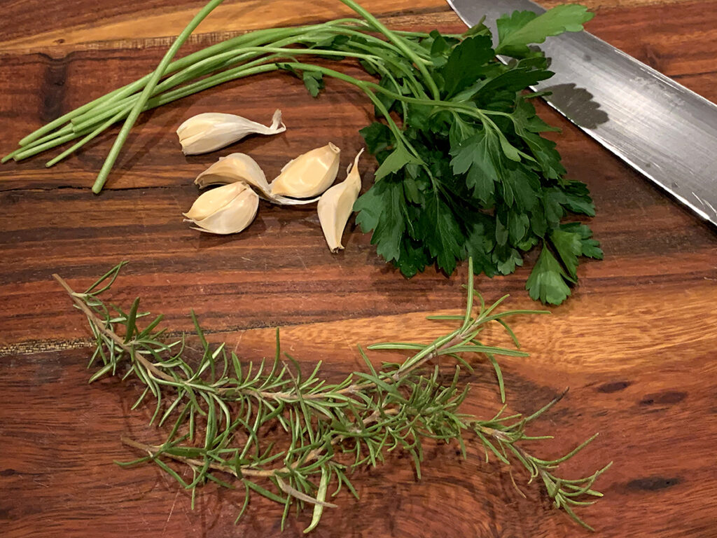 Fresh Parsley, rosemary and garlic cloves on a wood cutting board.
