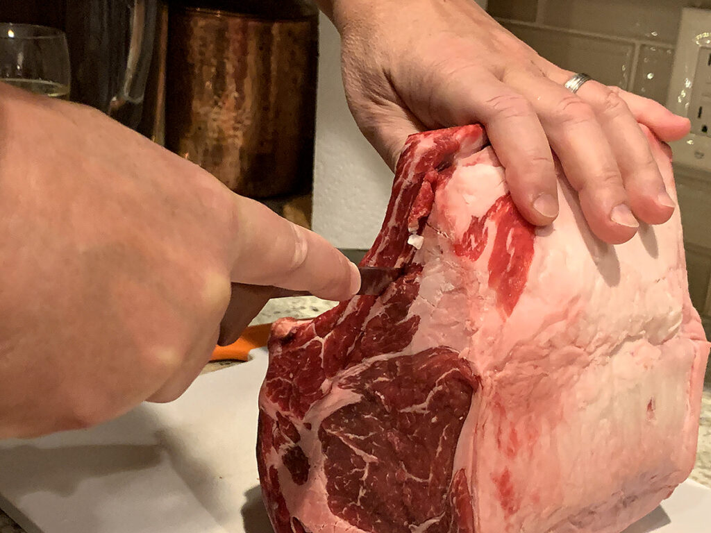 Hands with knife cutting the bones away from the rib roast.