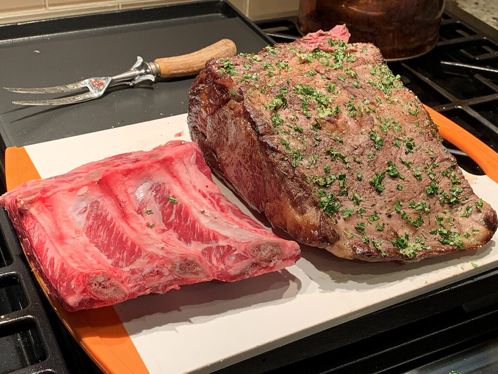 Seared and seasoned rib roast sitting next to the raw bones that was separated from the roast.