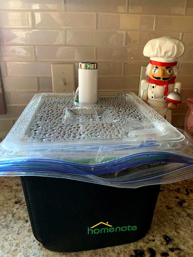 Large rectangular insulated container with sous vide device and lid. There's a nutcracker in the background who looks like a chef. 