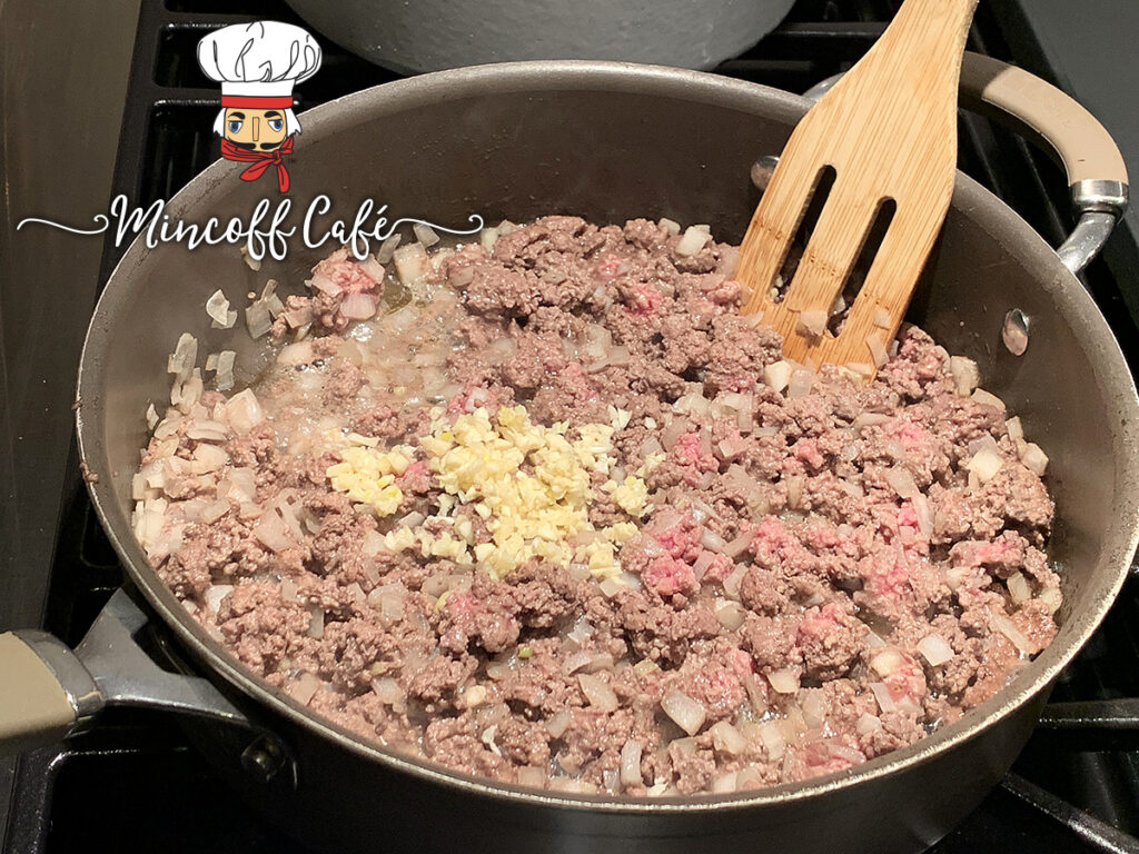 Mostly browned beef in a deep skillet with onions and garlic.