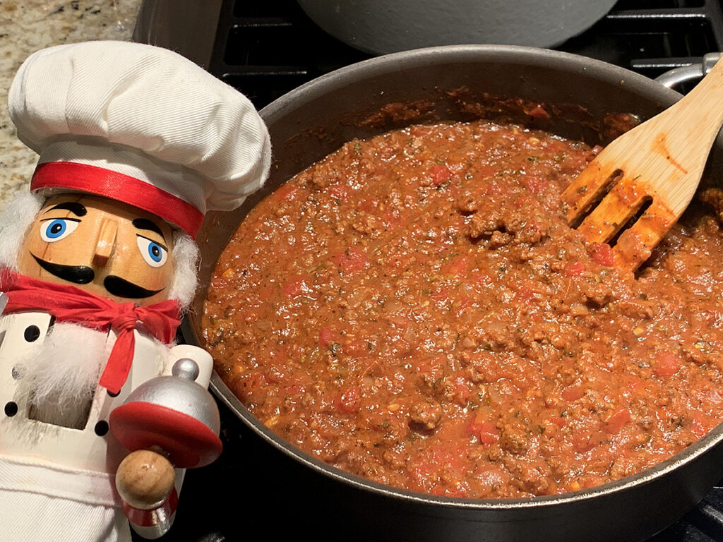 Meat and tomato sauce in a high skillet. There's a nutcracker in the foreground who looks like a chef.
