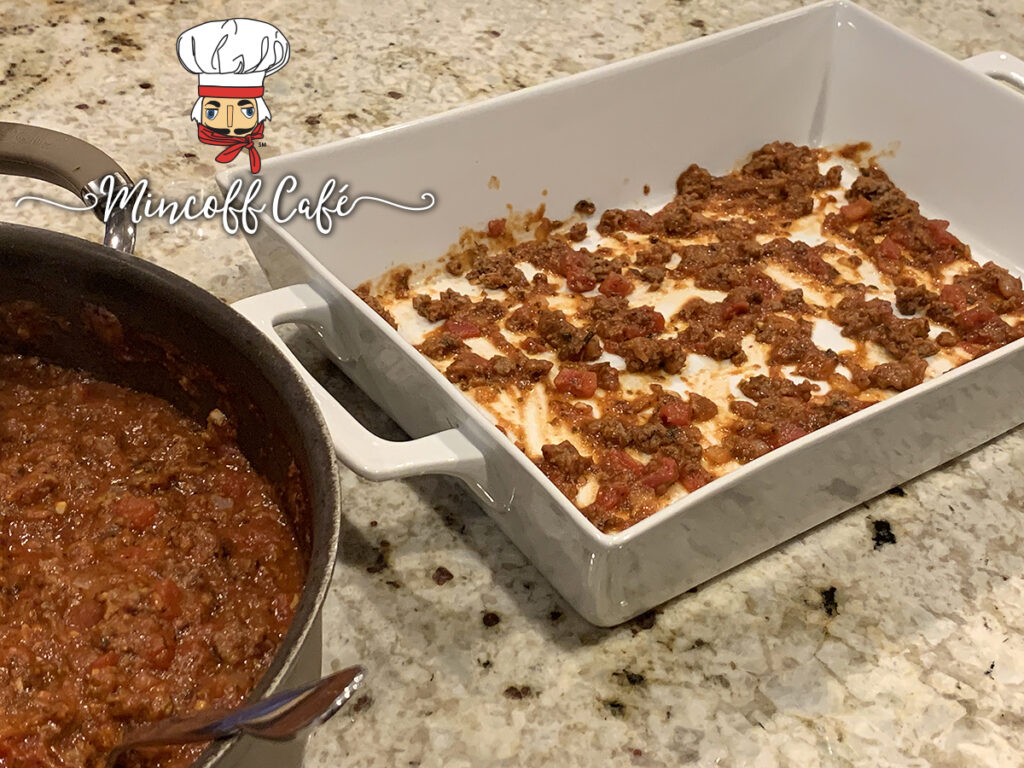 A thin layer of the red meat sauce is on the bottom of a white rectangular casserole dish.