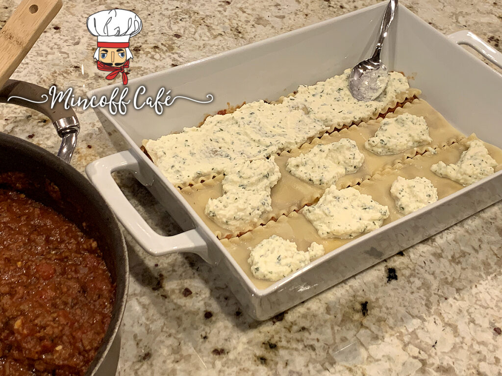 A single layer of sauce, lasagna noodles, and cheese filling in a white rectangular casserole dish. 
