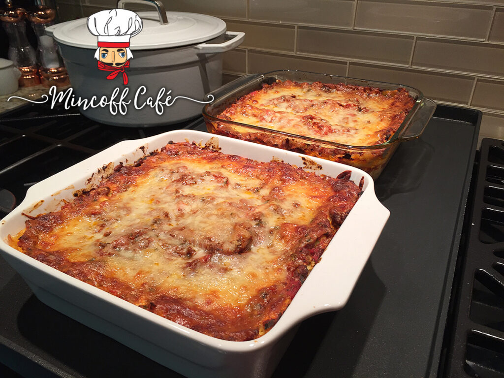 Two baked lasagnas in square casserole dishes sitting on the stove. 