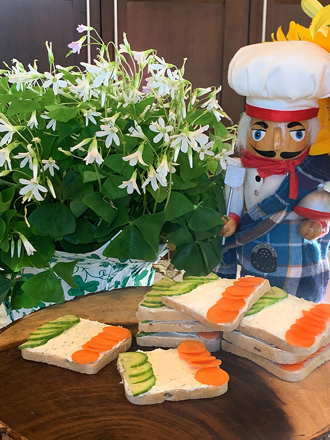 Tea sandwiches that resemble the Irish flag on a wooden platter. There's a nutcracker in the background that looks like a chef.
