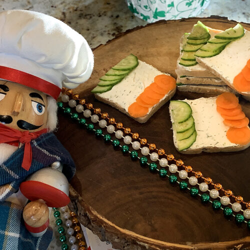 Tea sandwiches that resemble the Irish flag on a wooden platter. There's a nutcracker in the foreground that looks like a chef.