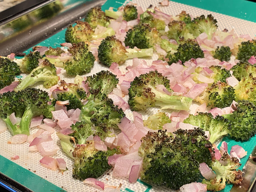 Roasted red onions and broccoli tops on a baking sheet.
