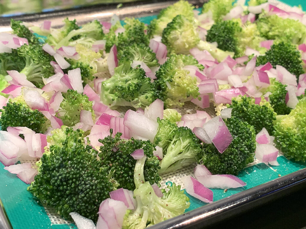 Chopped red onion and broccoli tops on a baking sheet. 