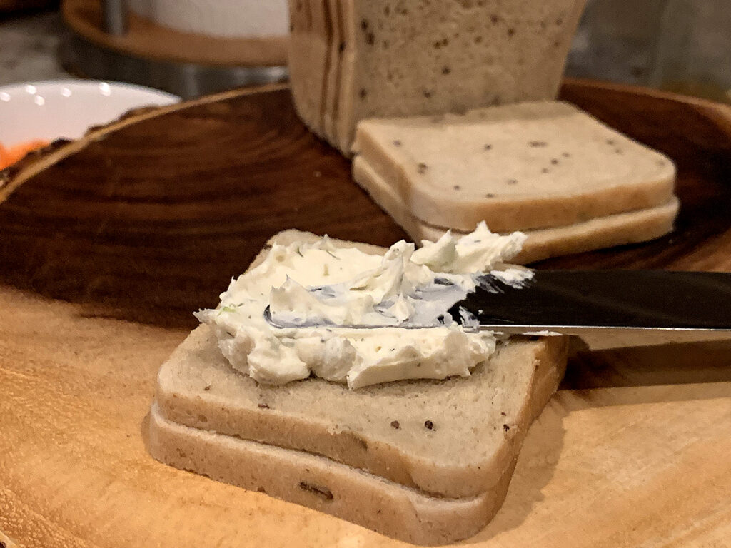 Butter knife spreading cream cheese blend onto mini party rye bread.