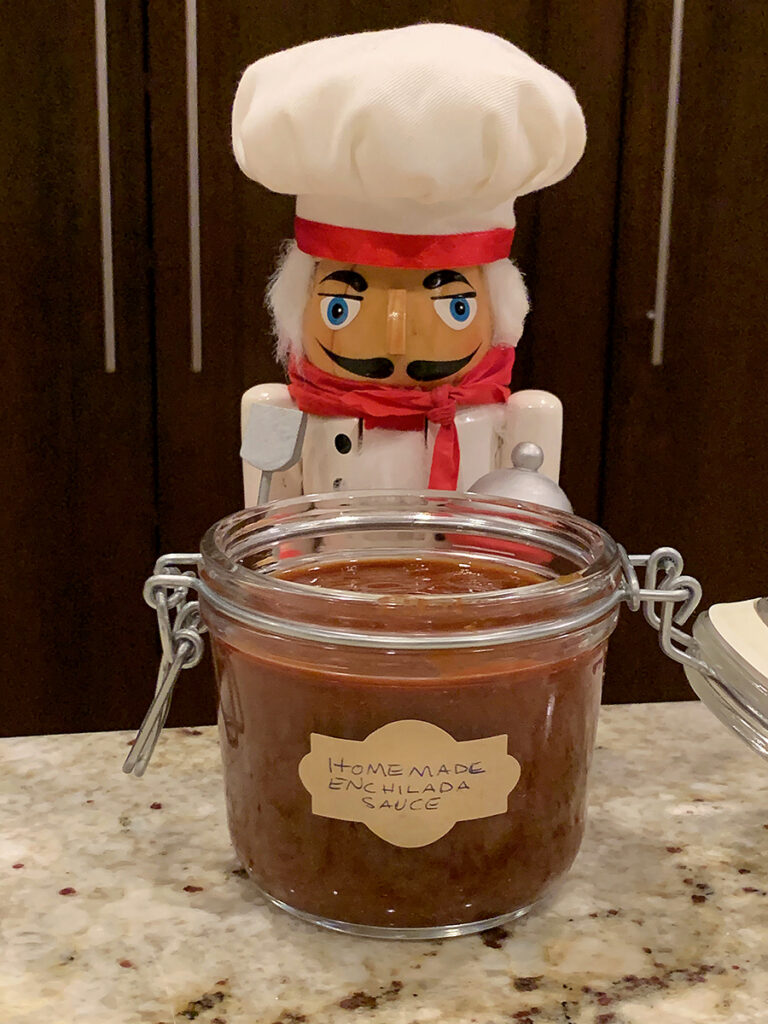 Red enchilada sauce in a glass jar with a hinged lid and a nutcracker who looks like a chef.