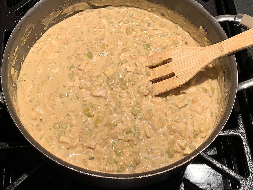 white enchiladas sauce with chicken and green chilies in a large skillet with a wooden spatula.