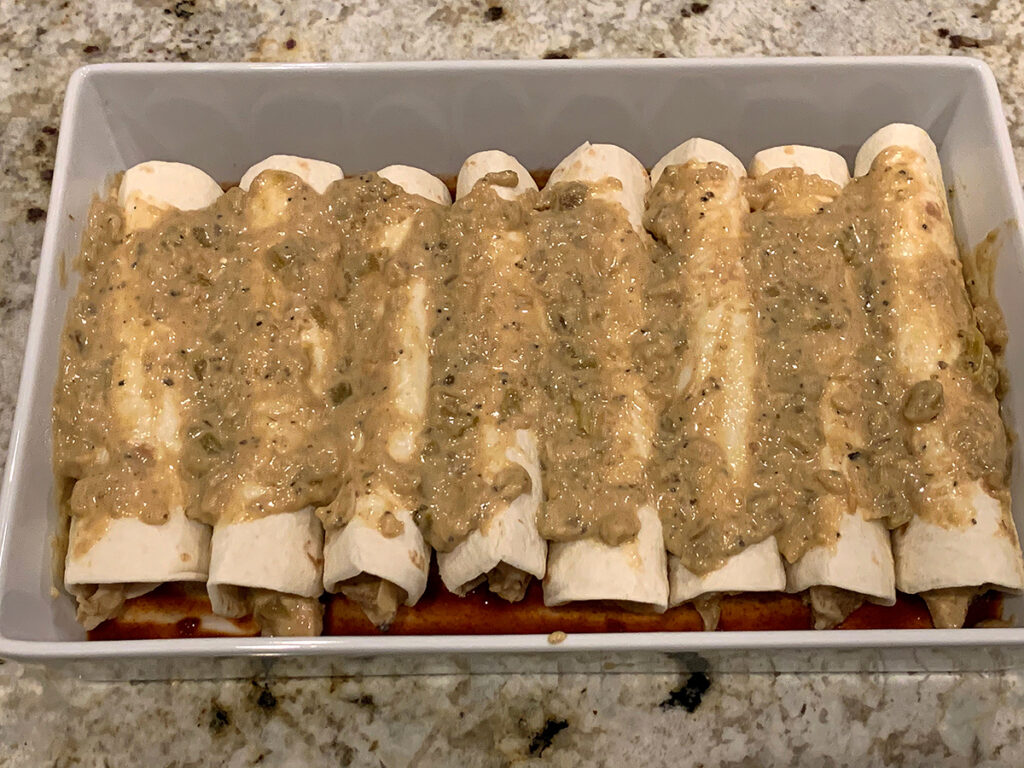 Eight rolled up tortillas neatly tucked into a casserole dish and topped with the white sauce.