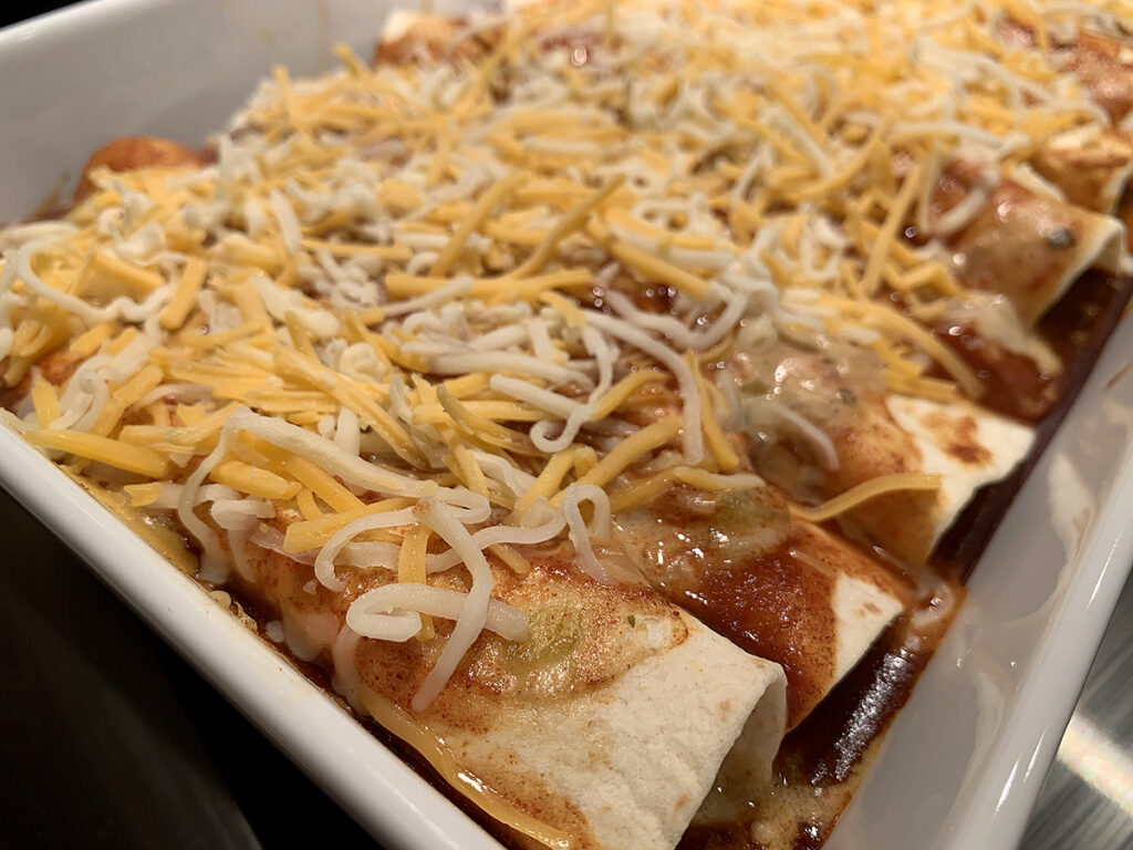 Eight rolled up tortillas neatly tucked into a casserole dish and topped with the cheese after baking.