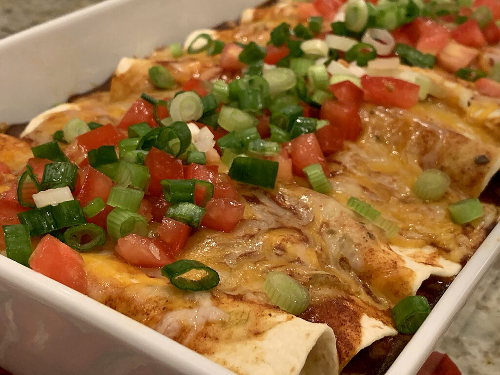 Cheesy and colorful chicken enchiladas in a rectangular white dish. 