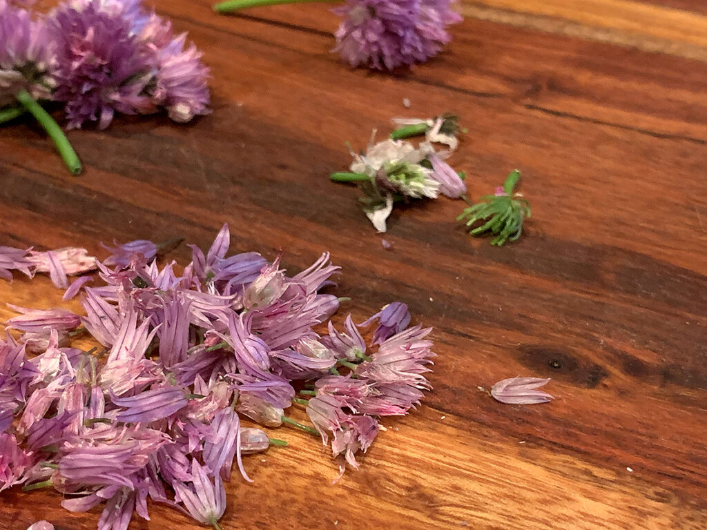 Pink chive petals laying on a beautiful wood board.