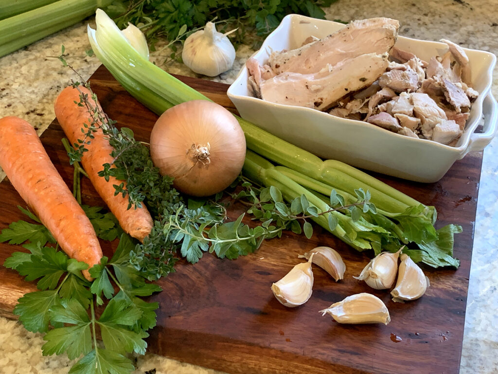 Carrots, celery, onion, garlic herbs and turkey on a wood board.