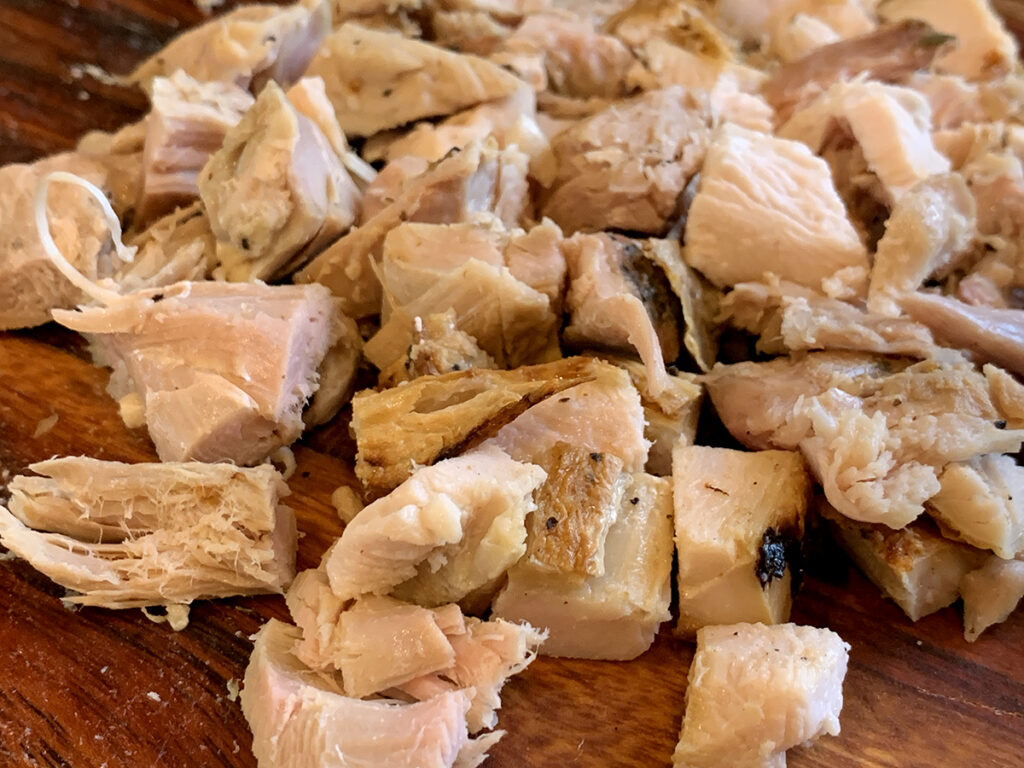 Cubed cooked turkey meat on a wood cutting board.