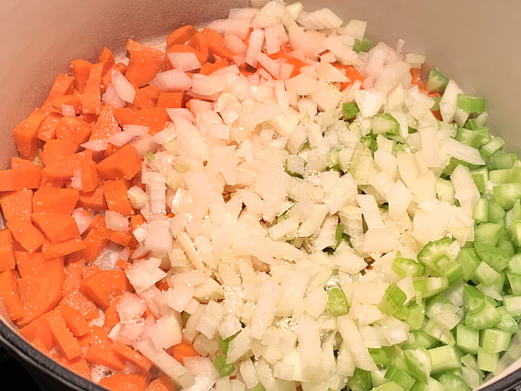 Carrots, celery and onions being sautéed in a white dutch oven. 