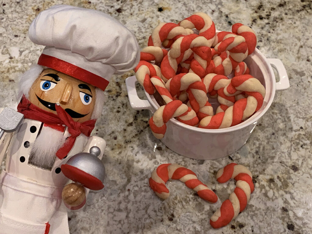 Red and white candy cane cookies in a white bowl with a nutcracker in the foreground who looks like a chef.
