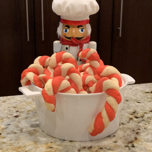 Red and white candy cane cookies in a white bowl with a nutcracker in the background who looks like a chef.