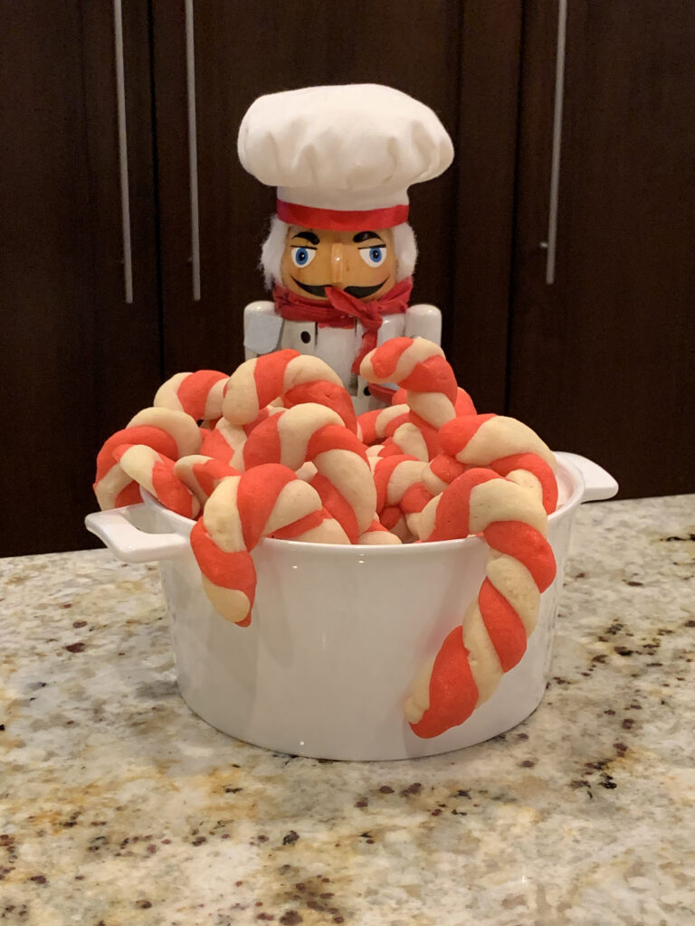 Red and white candy cane cookies in a white bowl with a nutcracker in the background who looks like a chef. 