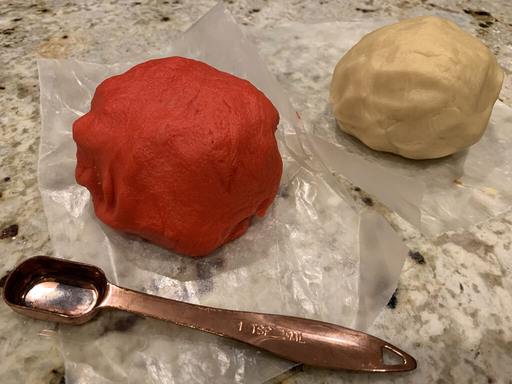 two balls of dough, one red and one white, and a copper 1/2 teaspoon measuring spoon.