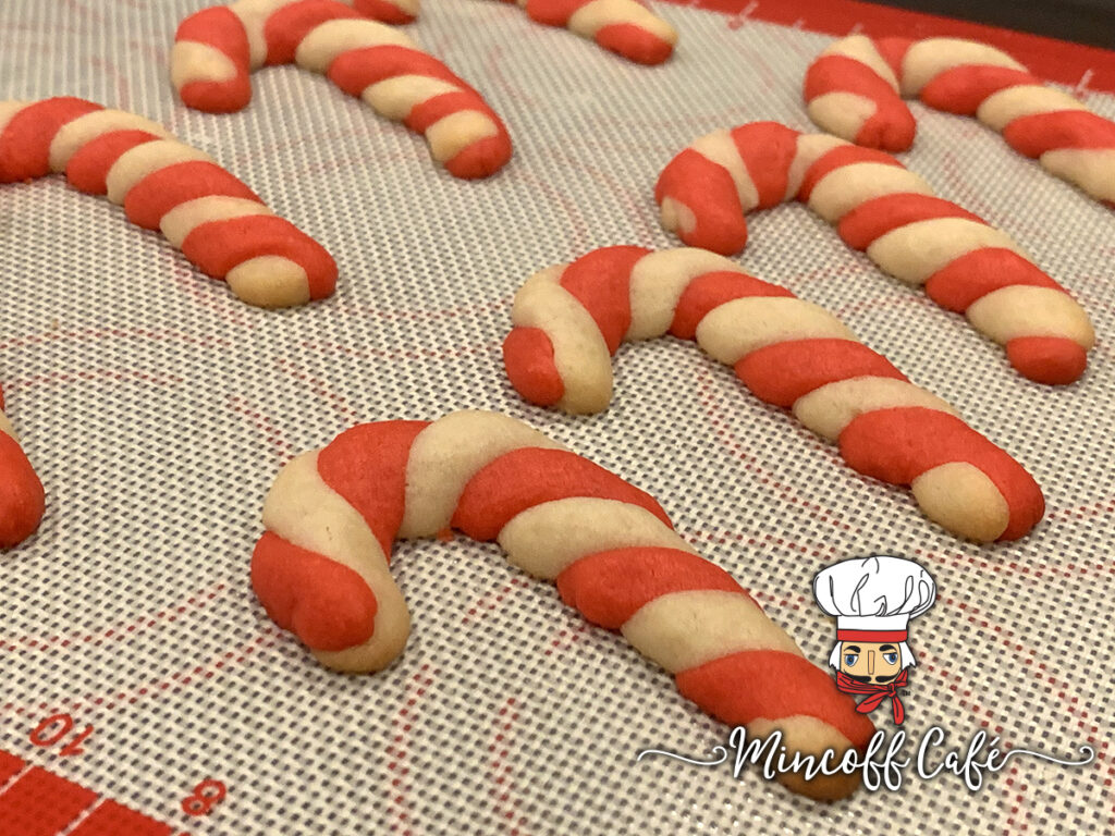 Baked red and white candy cane cookies on a silicone mat.