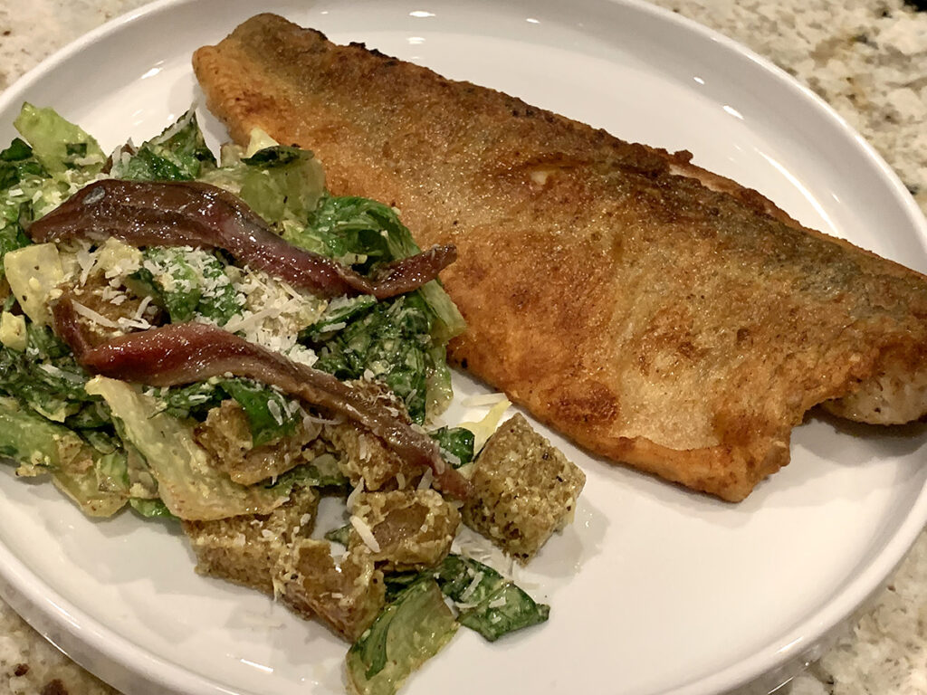 One crispy pan seared walleye fillet on a white plate with a Caesar salad.