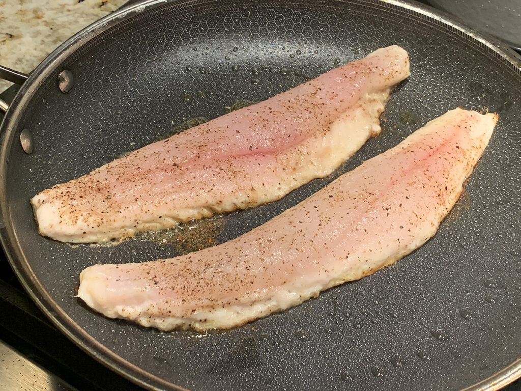 Two long pink fish fillets laying in a grey skillet.
