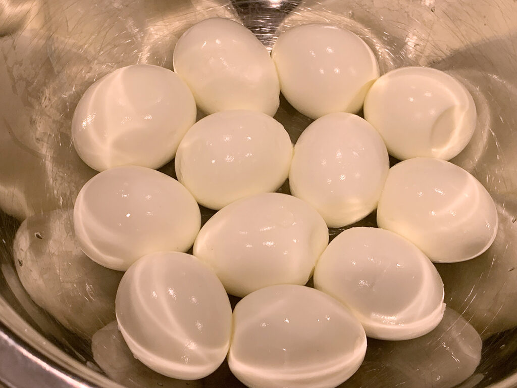 One dozen hard boiled eggs in a silver bowl.